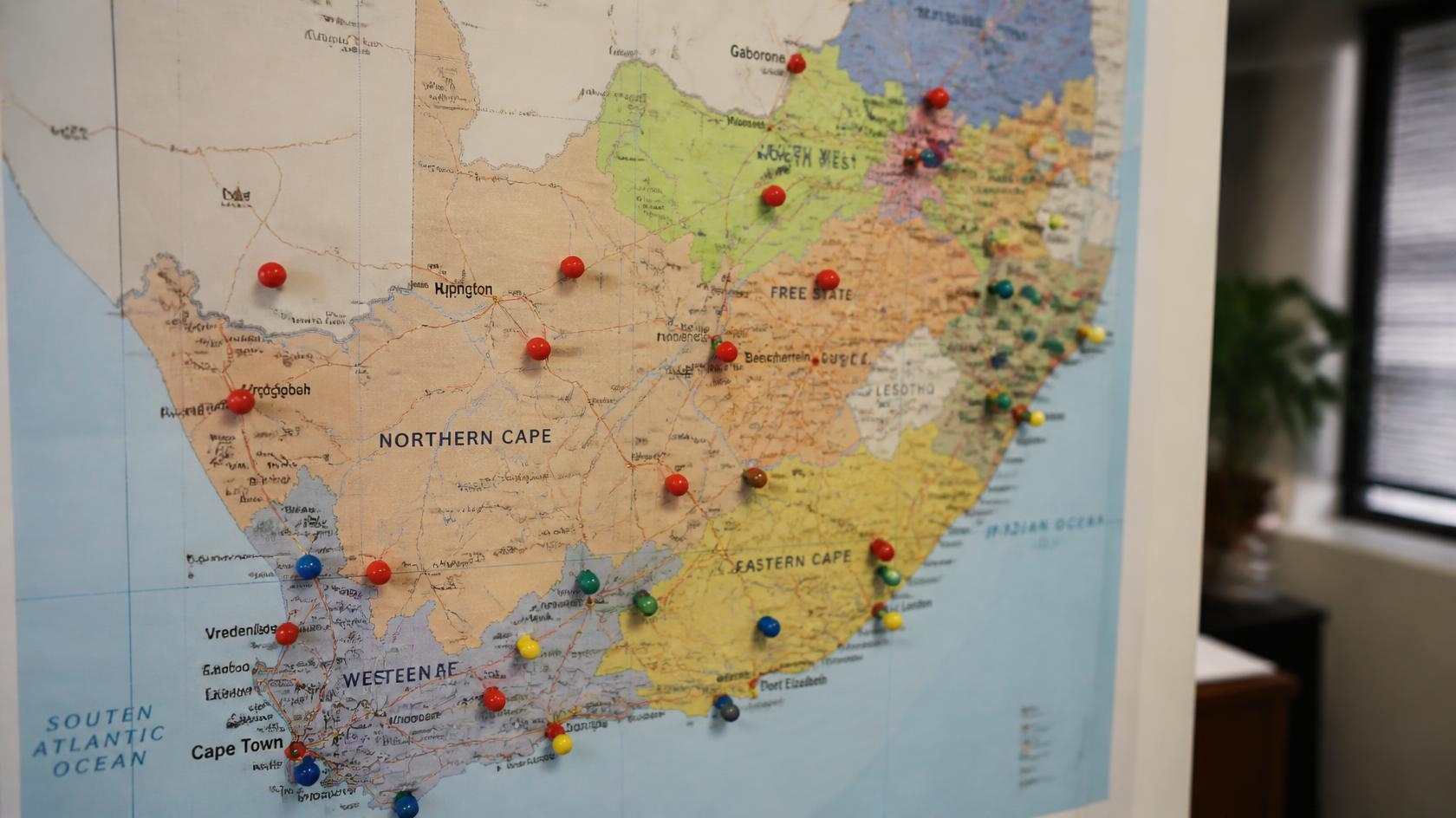 Professional photograph of a physical printed South African map on a desk or wall, colorful location pins and markers1111111